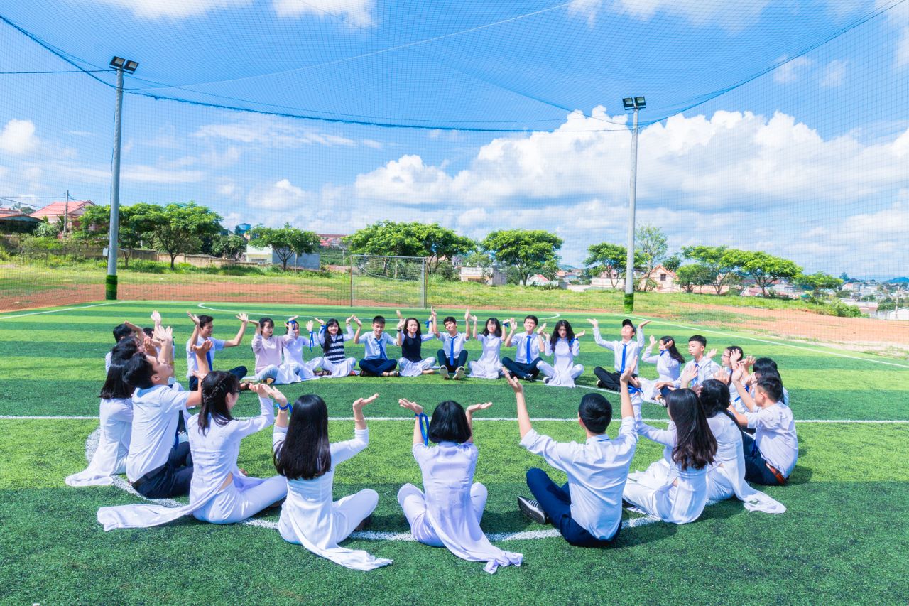A large group of young people sitting in a circle, engaging in an outdoor activity on a sunny day.