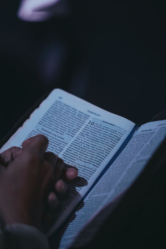 Close-up of hands holding an open book, deep in thought, in a dimly lit setting.